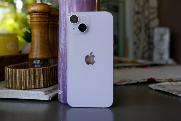 An iPhone 14 standing up on a table. Behind it is a purple water bottle.
