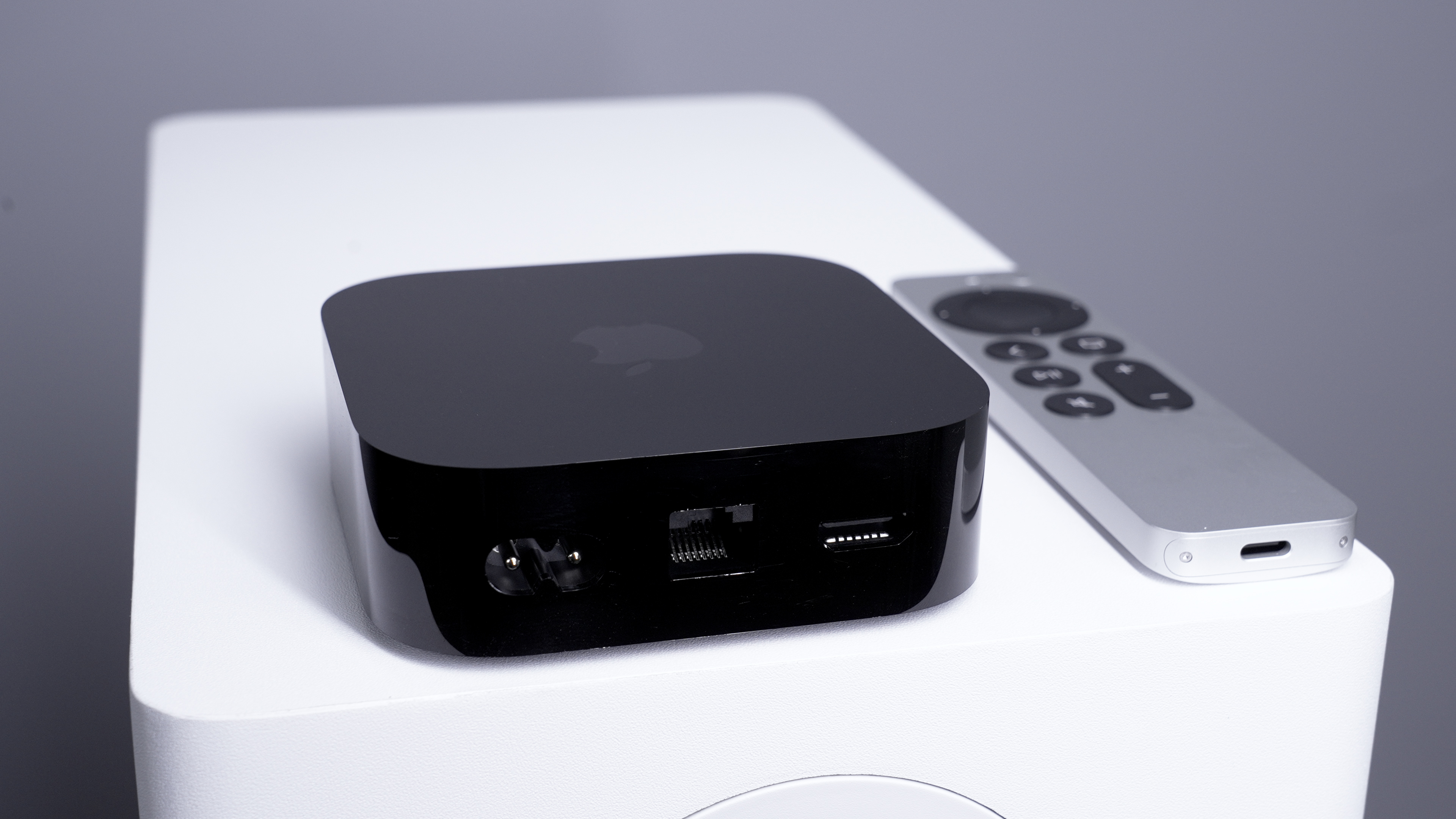 The rear view of an Apple TV 4K showing gigabit ethernet port, HDMI port, and power port, with the Siri remote alongside in the 
